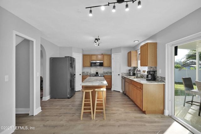 kitchen with arched walkways, light wood-style floors, appliances with stainless steel finishes, and a center island