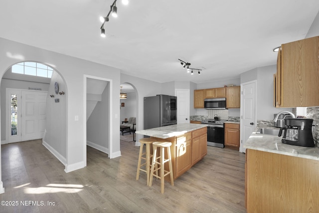 kitchen featuring arched walkways, a sink, stainless steel appliances, a kitchen breakfast bar, and a center island