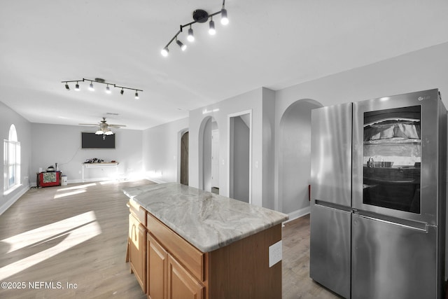 kitchen with a center island, arched walkways, refrigerator with glass door, and light wood-type flooring