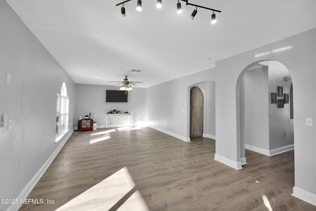 unfurnished living room with visible vents, a ceiling fan, wood finished floors, arched walkways, and baseboards