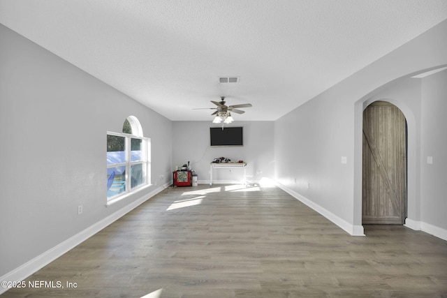 unfurnished living room featuring visible vents, a textured ceiling, wood finished floors, arched walkways, and ceiling fan