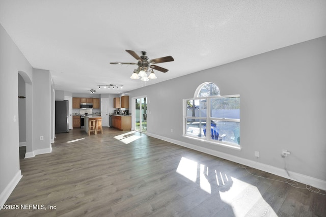 unfurnished living room featuring a ceiling fan, baseboards, arched walkways, dark wood-type flooring, and a textured ceiling