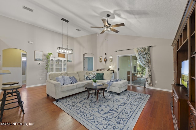 living area featuring visible vents, a textured ceiling, dark wood finished floors, arched walkways, and ceiling fan