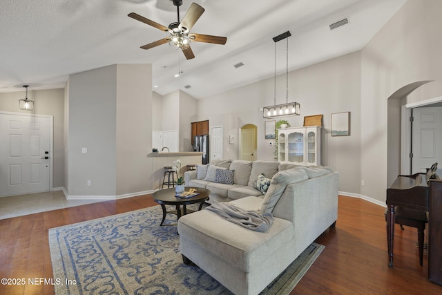 living room with dark wood finished floors, visible vents, arched walkways, and high vaulted ceiling