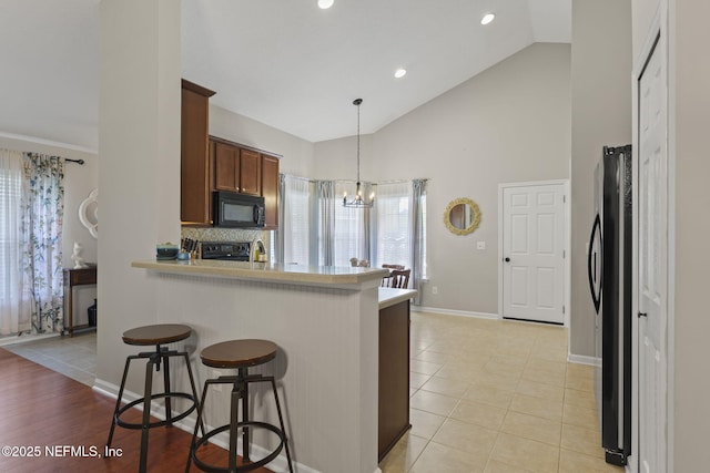 kitchen with light countertops, a kitchen breakfast bar, a peninsula, a notable chandelier, and black appliances