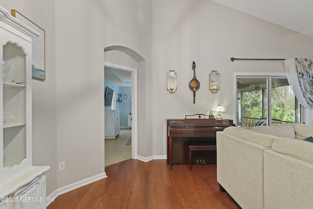 living area featuring baseboards, wood finished floors, arched walkways, and high vaulted ceiling