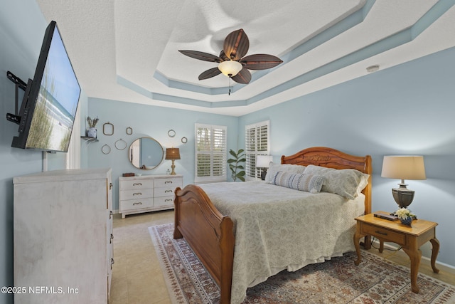 bedroom featuring light tile patterned floors, baseboards, ceiling fan, a textured ceiling, and a raised ceiling