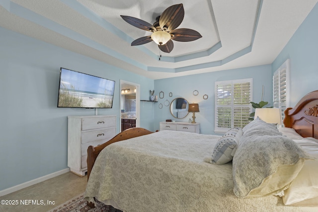 bedroom with ceiling fan, ensuite bath, a raised ceiling, and baseboards