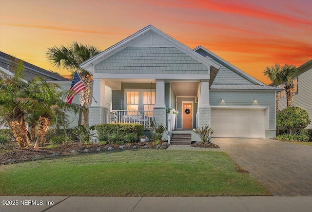 craftsman-style house with decorative driveway, a lawn, a porch, and an attached garage