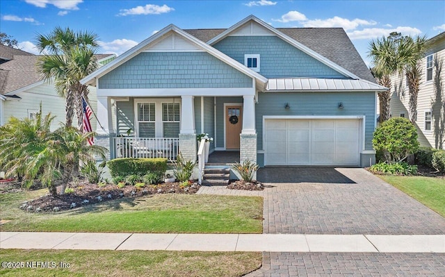 craftsman inspired home with a standing seam roof, decorative driveway, a porch, an attached garage, and metal roof