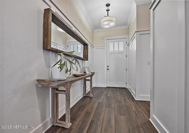 doorway with a wainscoted wall, dark wood-type flooring, crown molding, a decorative wall, and baseboards