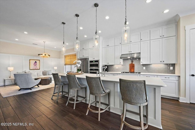 kitchen with under cabinet range hood, decorative backsplash, dark wood finished floors, and light countertops