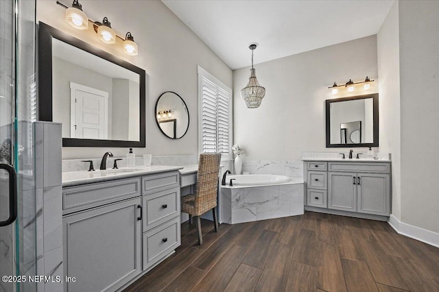 bathroom featuring a garden tub, two vanities, wood finished floors, and a sink