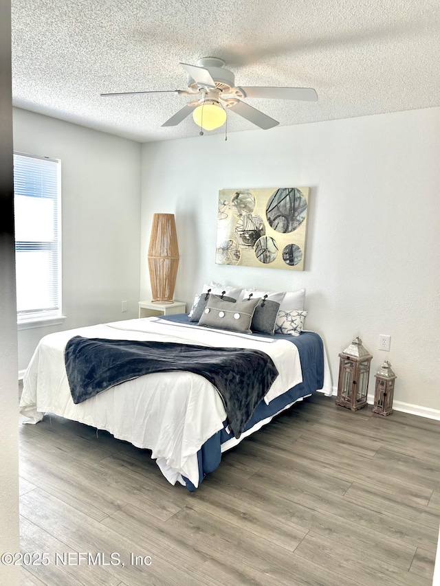 bedroom featuring baseboards, a textured ceiling, ceiling fan, and wood finished floors