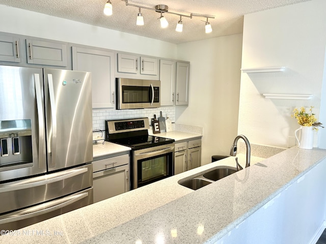 kitchen with light stone countertops, gray cabinets, a sink, stainless steel appliances, and backsplash