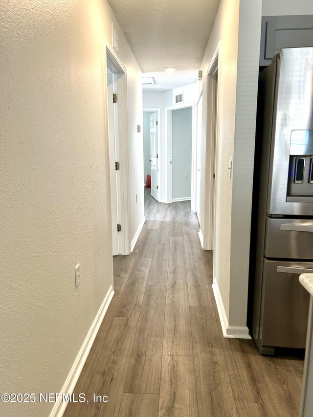 corridor with visible vents, a textured ceiling, dark wood finished floors, baseboards, and a textured wall