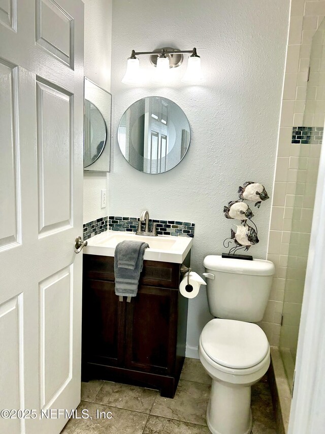 full bathroom with toilet, backsplash, a tile shower, tile patterned flooring, and vanity