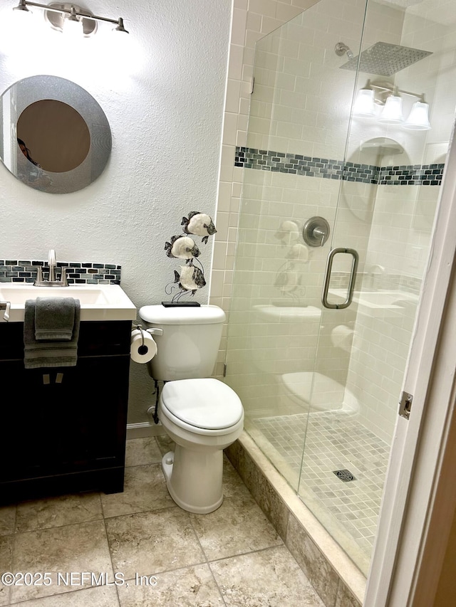 bathroom with toilet, a stall shower, baseboards, vanity, and a textured wall