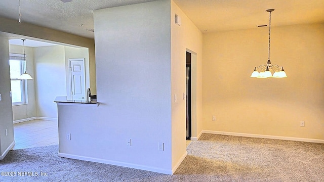 carpeted empty room with a textured ceiling, baseboards, and a chandelier