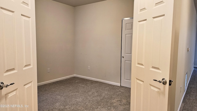 unfurnished room with baseboards and dark colored carpet