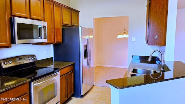 kitchen with dark stone counters, appliances with stainless steel finishes, a peninsula, brown cabinetry, and a sink