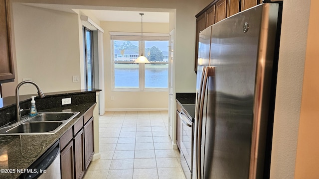 kitchen with a sink, stainless steel appliances, dark stone counters, light tile patterned floors, and hanging light fixtures