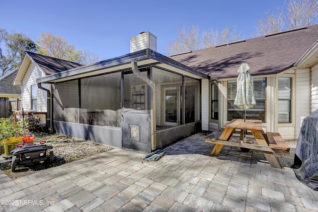 back of property featuring a sunroom, roof with shingles, a patio, and a chimney