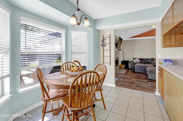 dining room featuring lofted ceiling, light tile patterned flooring, a notable chandelier, a fireplace, and baseboards