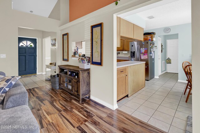 kitchen featuring light wood-style flooring, baseboards, light countertops, light brown cabinetry, and stainless steel fridge