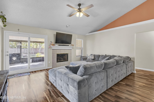 living area featuring ceiling fan, vaulted ceiling, wood finished floors, a tile fireplace, and baseboards