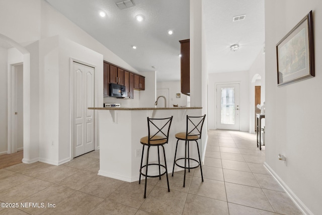 kitchen featuring arched walkways, black microwave, visible vents, and a breakfast bar area