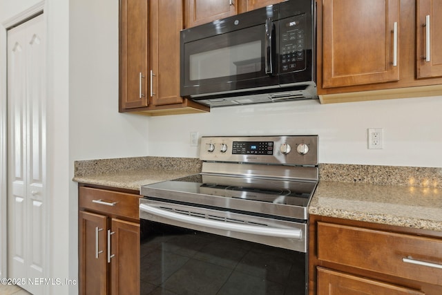 kitchen with light stone countertops, stainless steel electric stove, black microwave, and brown cabinetry