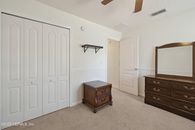 bedroom featuring ceiling fan, a textured ceiling, light carpet, visible vents, and a closet