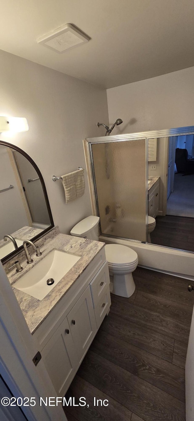 bathroom with bath / shower combo with glass door, wood finished floors, vanity, and toilet