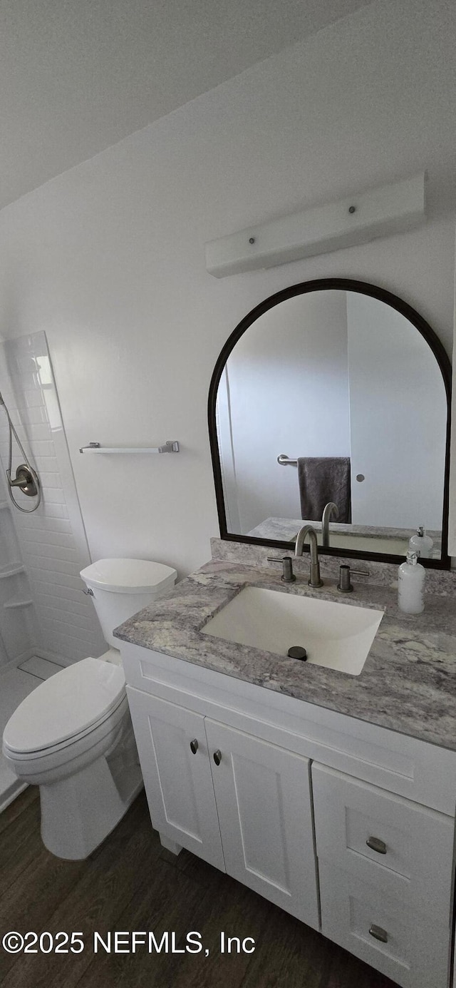 bathroom featuring a tile shower, wood finished floors, vanity, and toilet