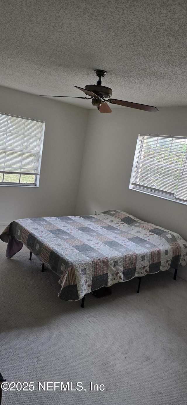 unfurnished bedroom with a textured ceiling, carpet floors, and a ceiling fan