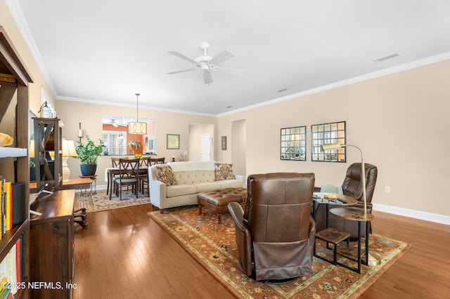 living room featuring wood finished floors, baseboards, visible vents, ceiling fan, and ornamental molding