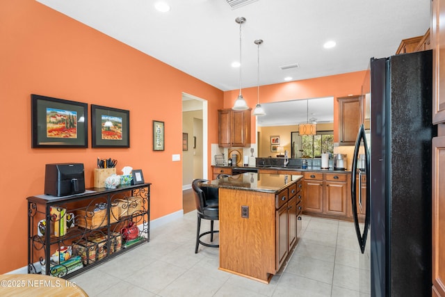 kitchen with visible vents, brown cabinets, a sink, freestanding refrigerator, and a breakfast bar area