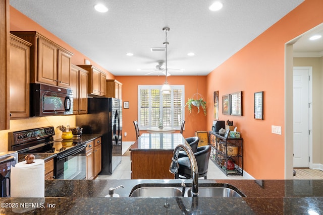 kitchen featuring brown cabinetry, visible vents, a sink, black appliances, and a center island