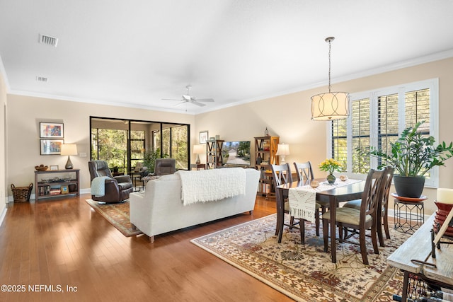 living area with visible vents, baseboards, ornamental molding, wood finished floors, and a ceiling fan