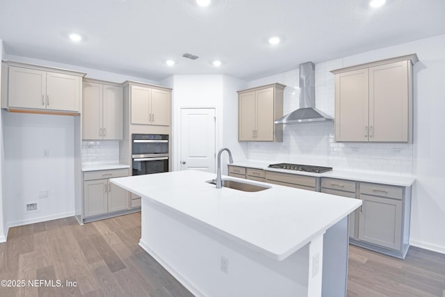 kitchen featuring gray cabinetry, wall chimney range hood, and a sink