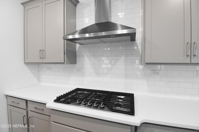 kitchen with backsplash, gray cabinetry, light countertops, stainless steel gas stovetop, and wall chimney exhaust hood