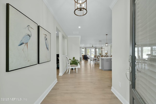 hallway featuring a chandelier, light wood-type flooring, crown molding, and baseboards