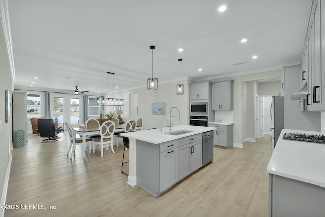 kitchen with an island with sink, appliances with stainless steel finishes, gray cabinets, crown molding, and a sink