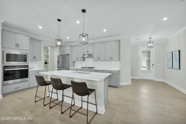 kitchen with appliances with stainless steel finishes, a kitchen breakfast bar, light countertops, gray cabinetry, and under cabinet range hood