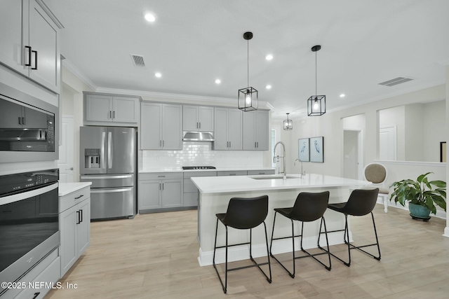 kitchen featuring under cabinet range hood, a sink, visible vents, appliances with stainless steel finishes, and gray cabinets