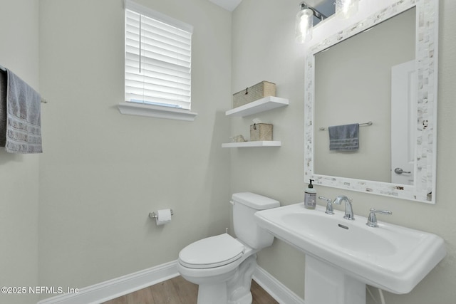 half bath with toilet, baseboards, a sink, and wood finished floors