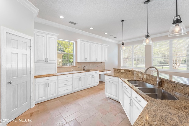 kitchen featuring visible vents, decorative light fixtures, ornamental molding, white cabinetry, and a sink