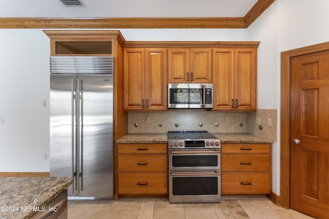 kitchen featuring stainless steel appliances, light stone countertops, and brown cabinetry