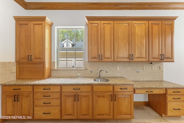 kitchen featuring decorative backsplash, brown cabinets, light stone countertops, and a sink